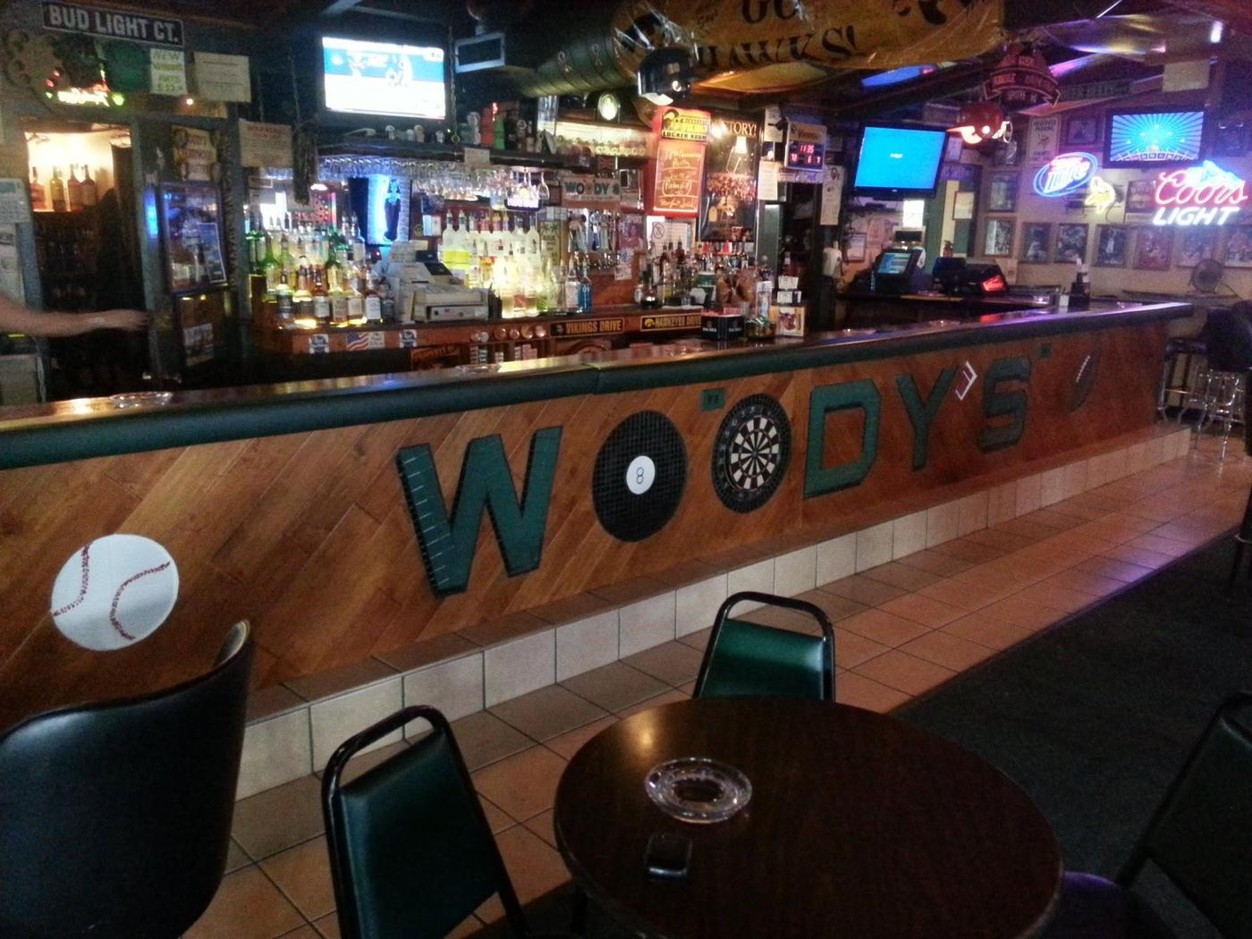 The front of the bar with WOODY'S set in green relief letters, an eight ball and a dartboard for the two Os