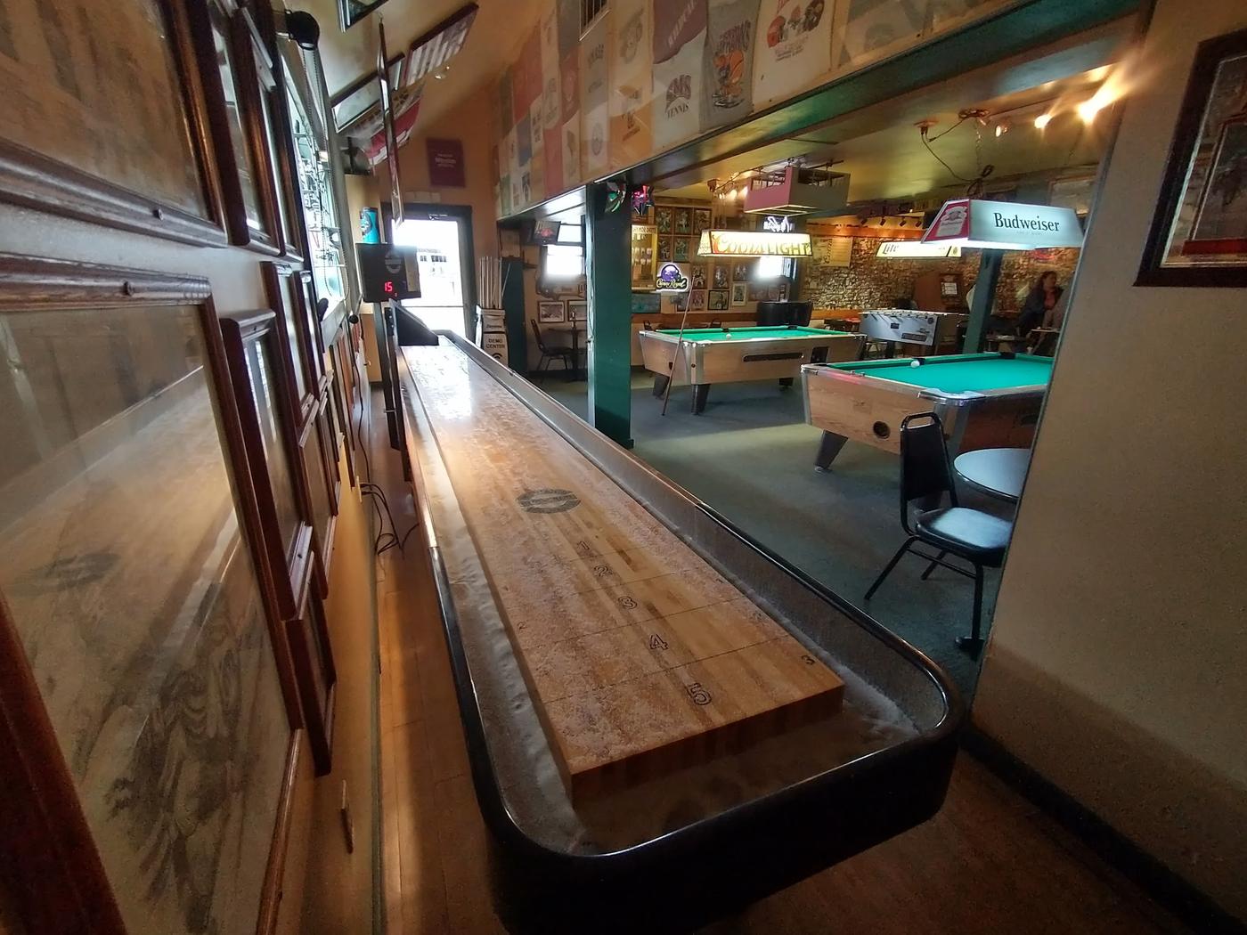 The shuffleboard table running down the room with two pool tables and the foosball table behind it