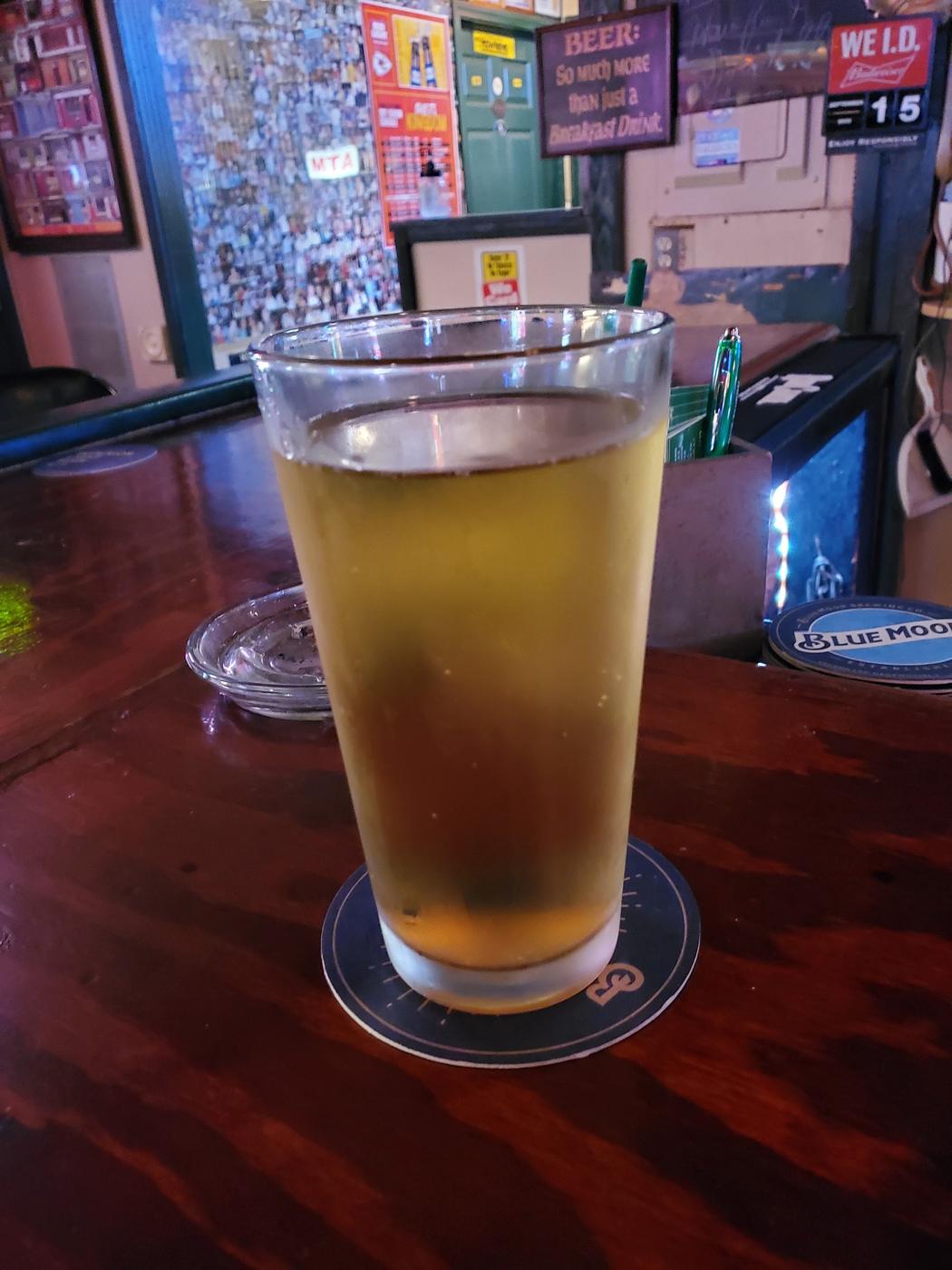 A cold pint sitting on the wooden bar top with the photo wall behind it